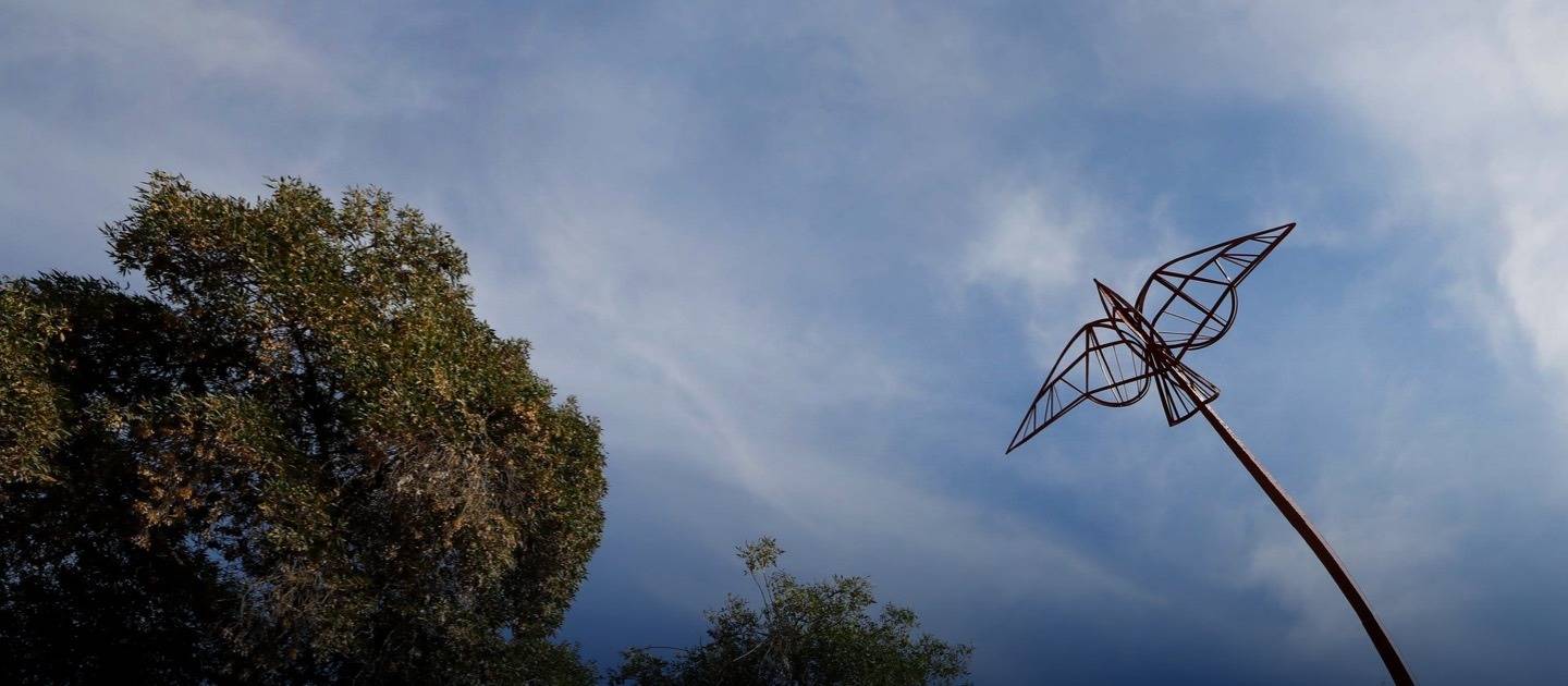 Escultura de una ave elevada entre árboles y cielo.
