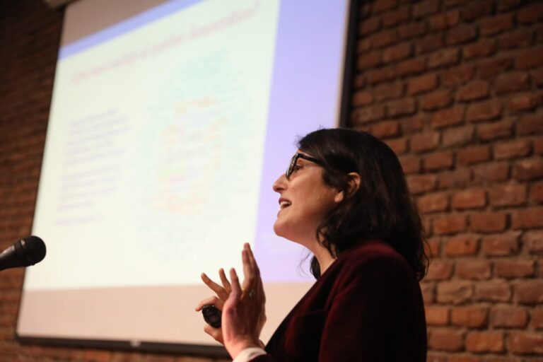 Oradora hablando en un evento con fondo de ladrillo.
